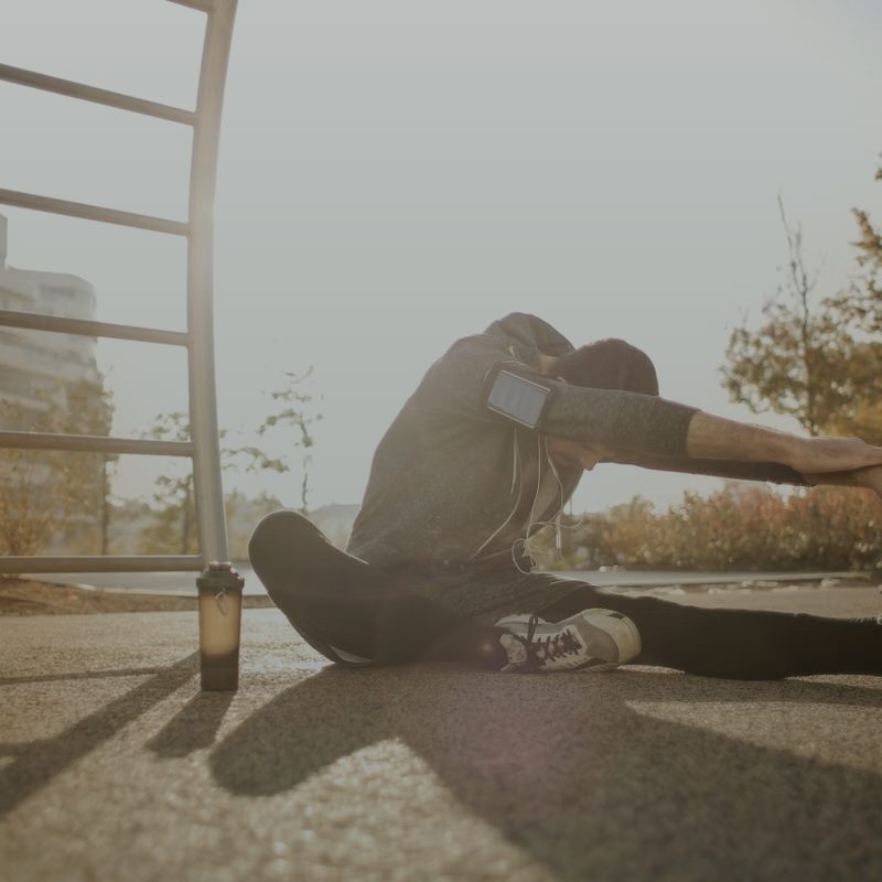 An athlete in a low seated stretch, warm backlight behind