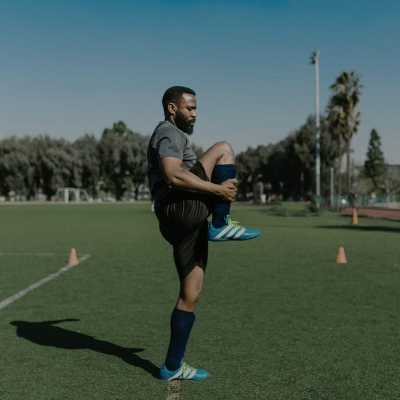 An athlete in dark sportswear stretching on a grass field