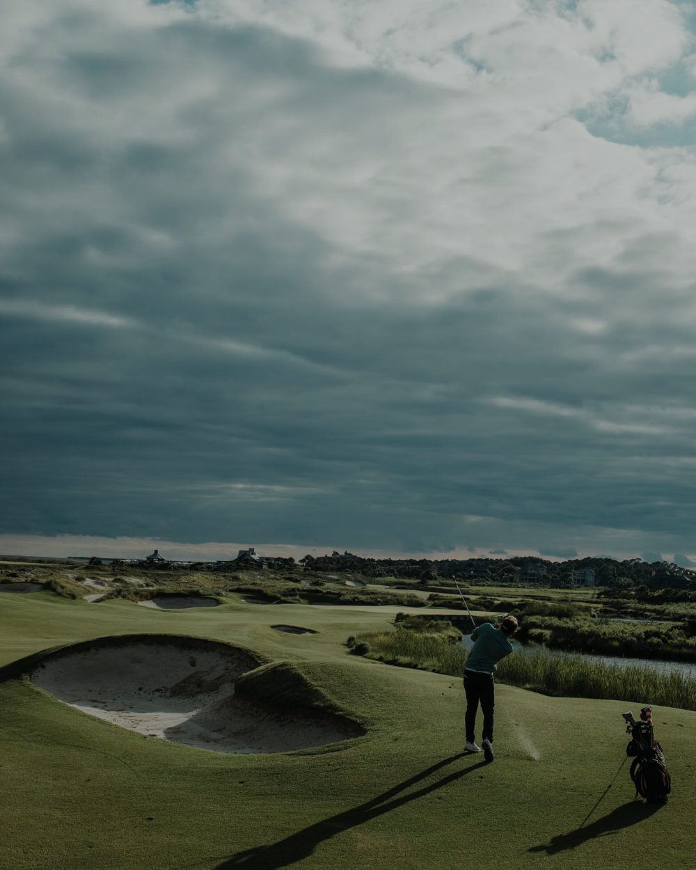 A lone golfer walking a links fairway under a wide, cloud-heavy sky